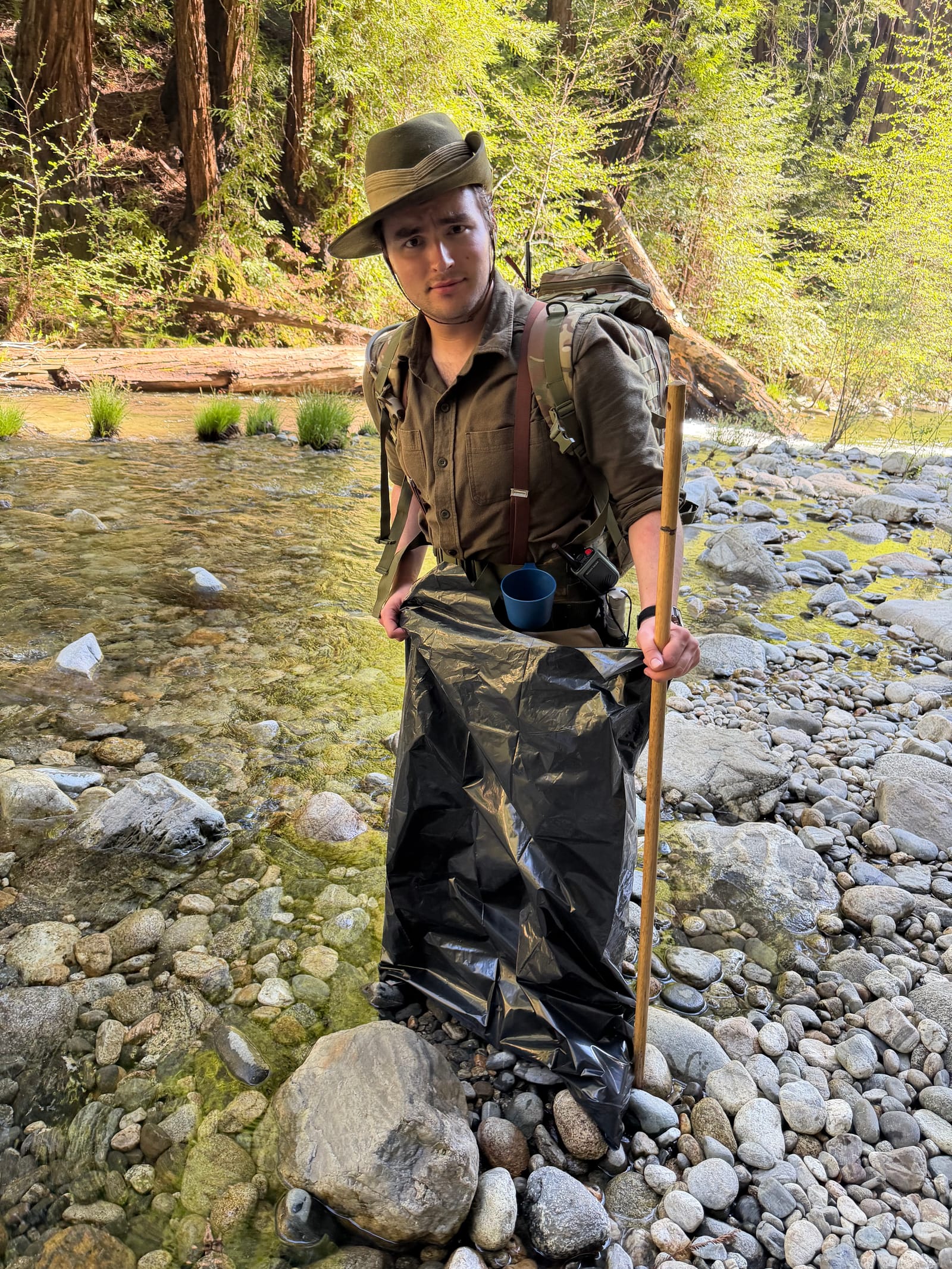 Stephen Weinstock crossing a creek in the redwoods with a backpack and walking stick