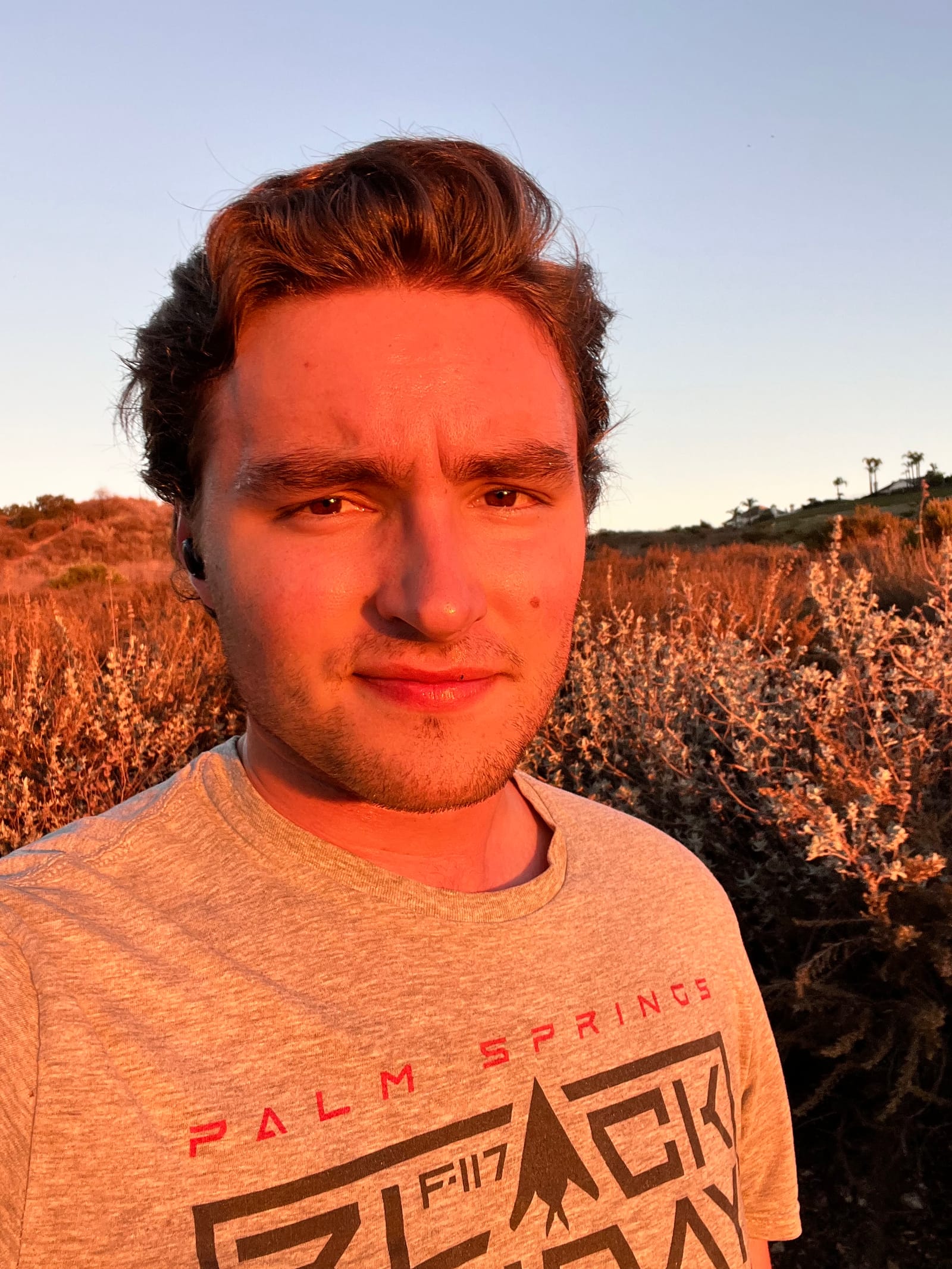 Stephen Weinstock in a grey T-shirt, lit by the setting sun, with dry brush behind him