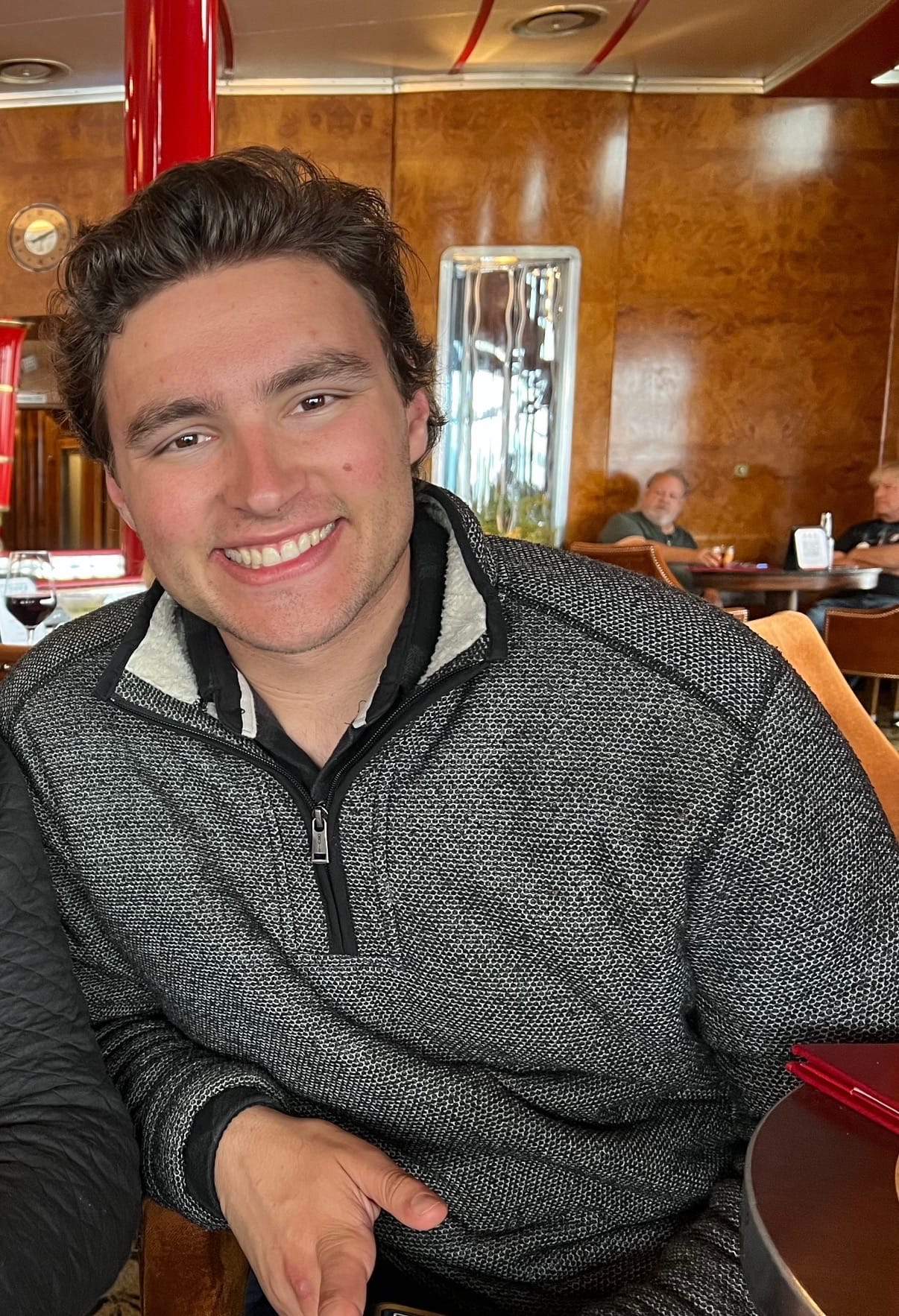 Stephen Weinstock smiling at a table in a wood-panelled restaurant, wearing a grey zip-neck pullover